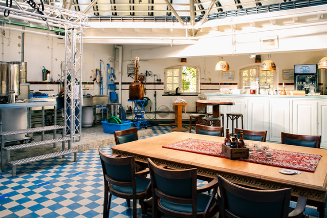 Proeflokaal en brouwruimte van Brouwerij Rolduc met een grote houten tafel, stoelen, bar en zicht op de brouwapparatuur.